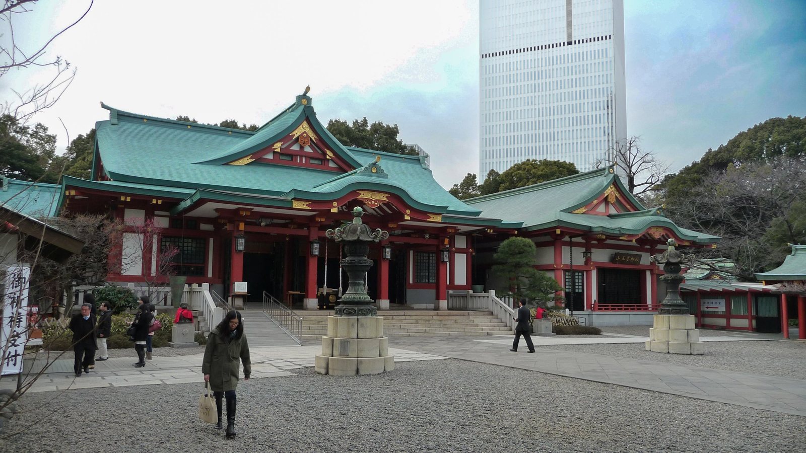 Hauptgebäude des Hie-jinja mit grünen Dächern und roten Säulen, dahinter ein weißer Büroturm
