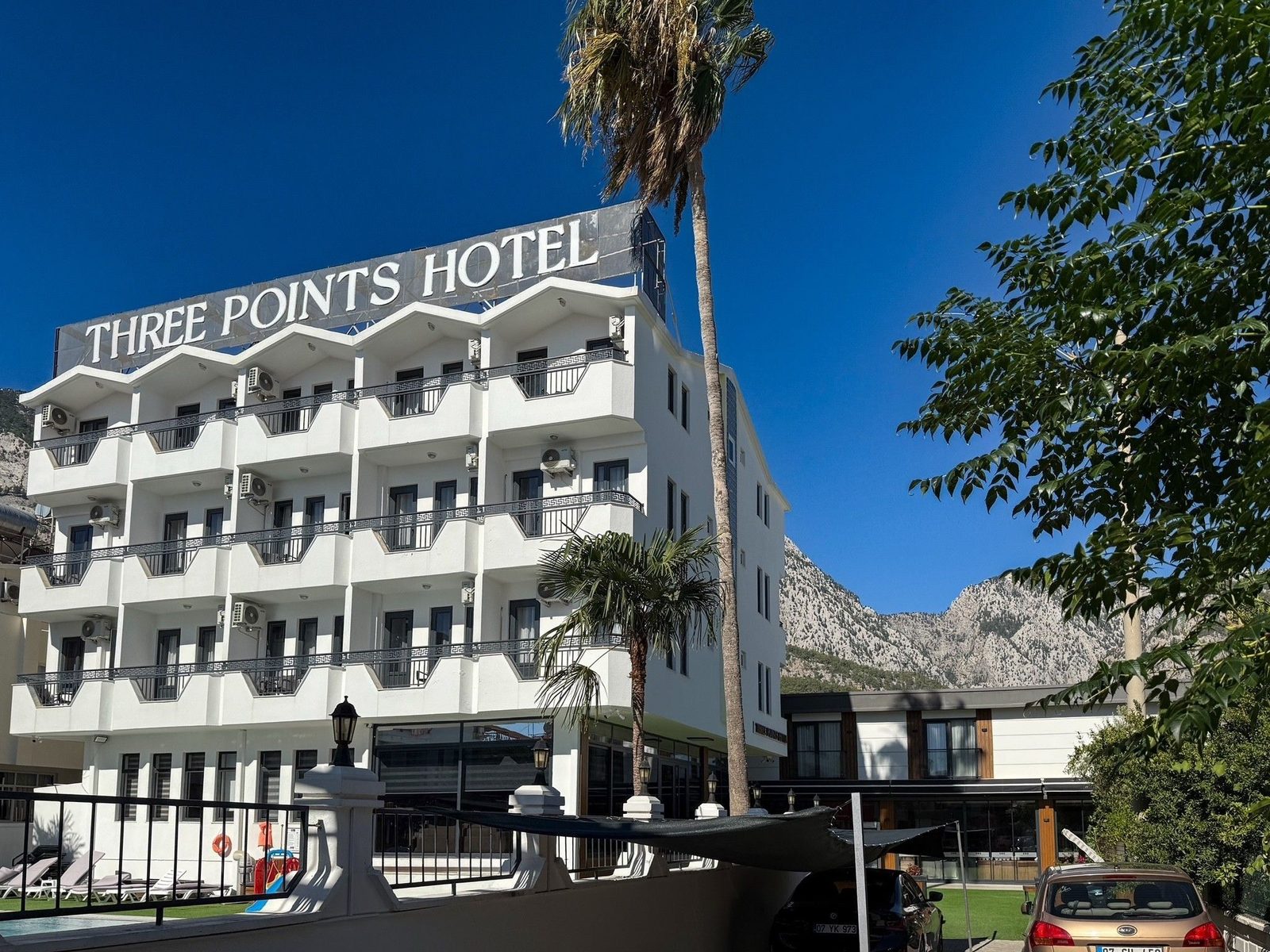 Weißes Hotelgebäude mit Balkonen und Palmen vor den Taurus-Bergen in Beldibi