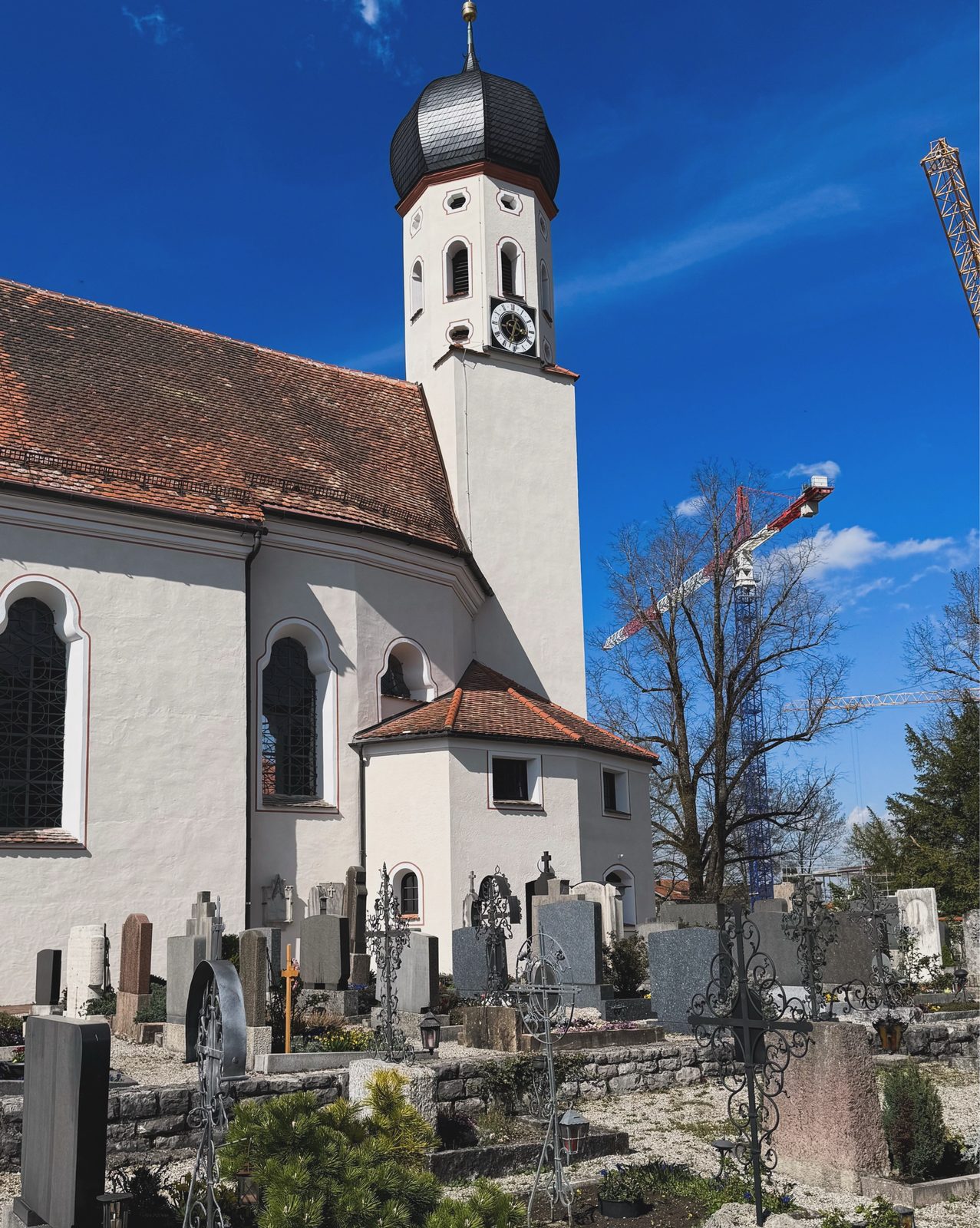 Pfarrkirche von Bad Heilbrunn mit Zwiebelturm und altem Friedhof unter blauem Himmel