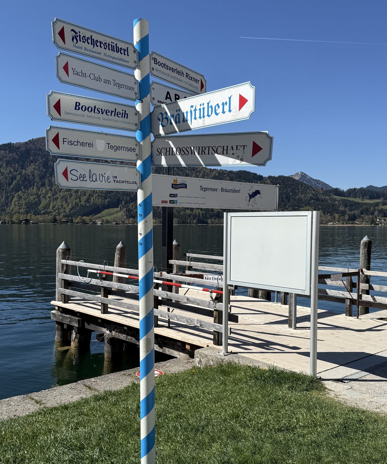 Blau-weiß gestreifter Schilderbaum am Tegernsee mit Wegweisern zu Bräustüberl und Fischerstüberl