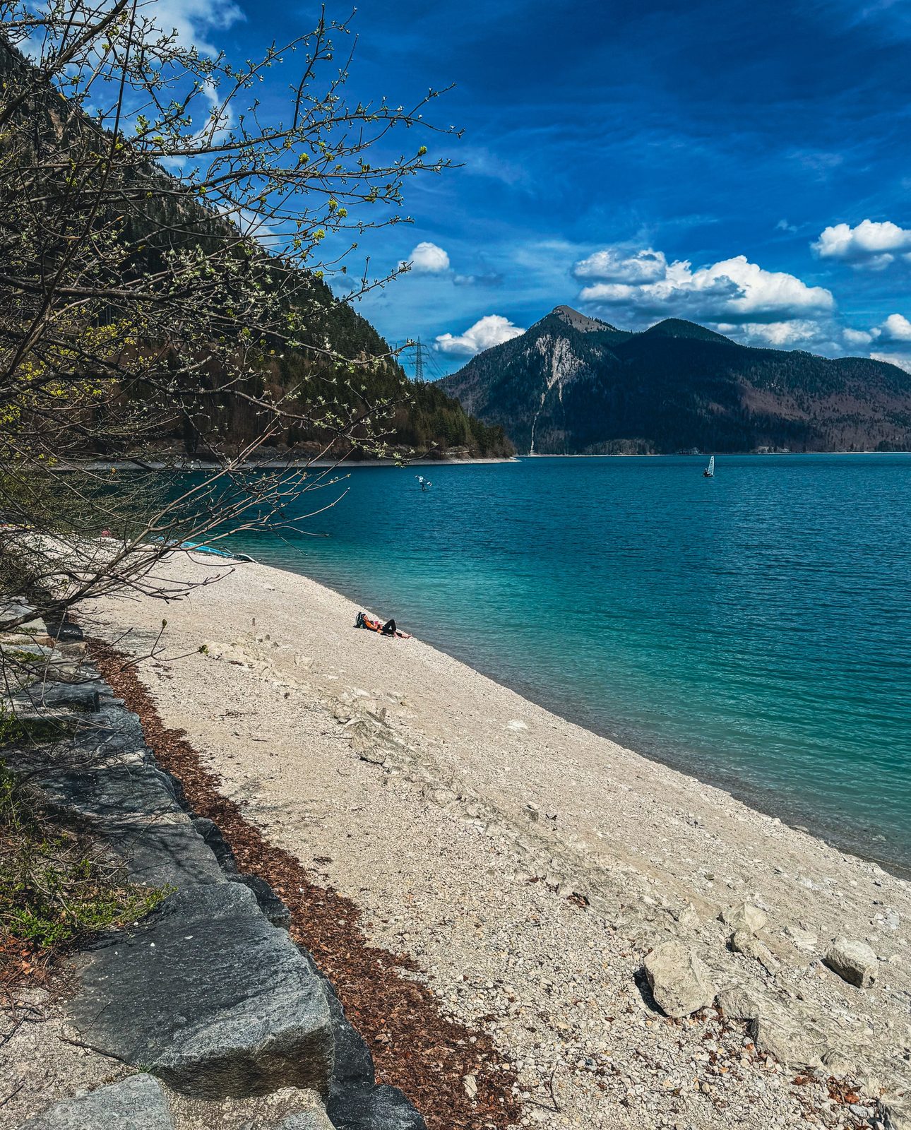 Türkisfarbene Kiesbucht am Walchensee mit Bergpanorama und einsamem Segler