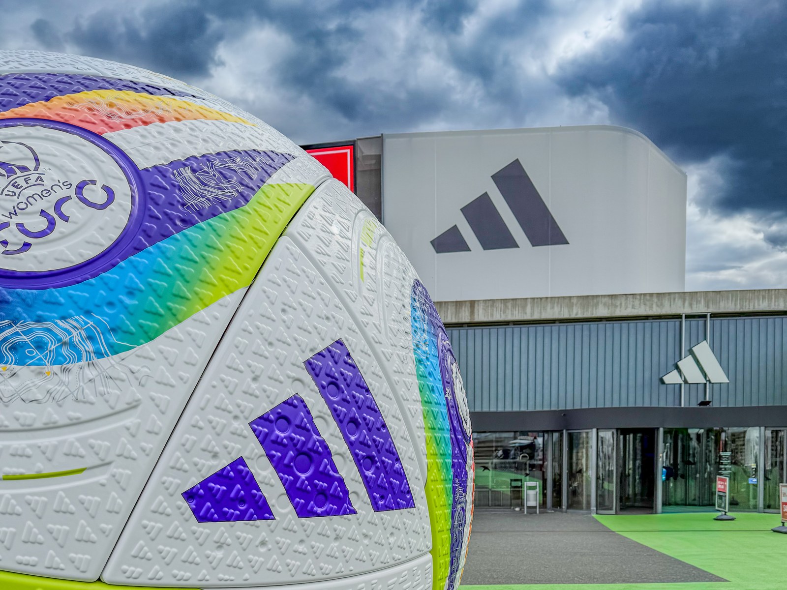 Adidas-Logo an einem Gebäude, im Vordergrund ein Fußball der UEFA Women's Euro