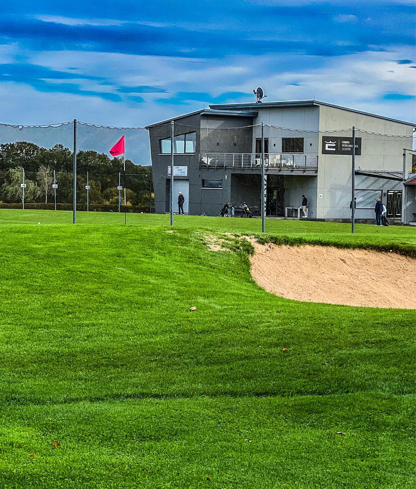 Cobra Performance Center am Übungsgelände des Golf-Club Herzogenaurach, im Vordergrund Bunker und rote Fahne auf dem Grün