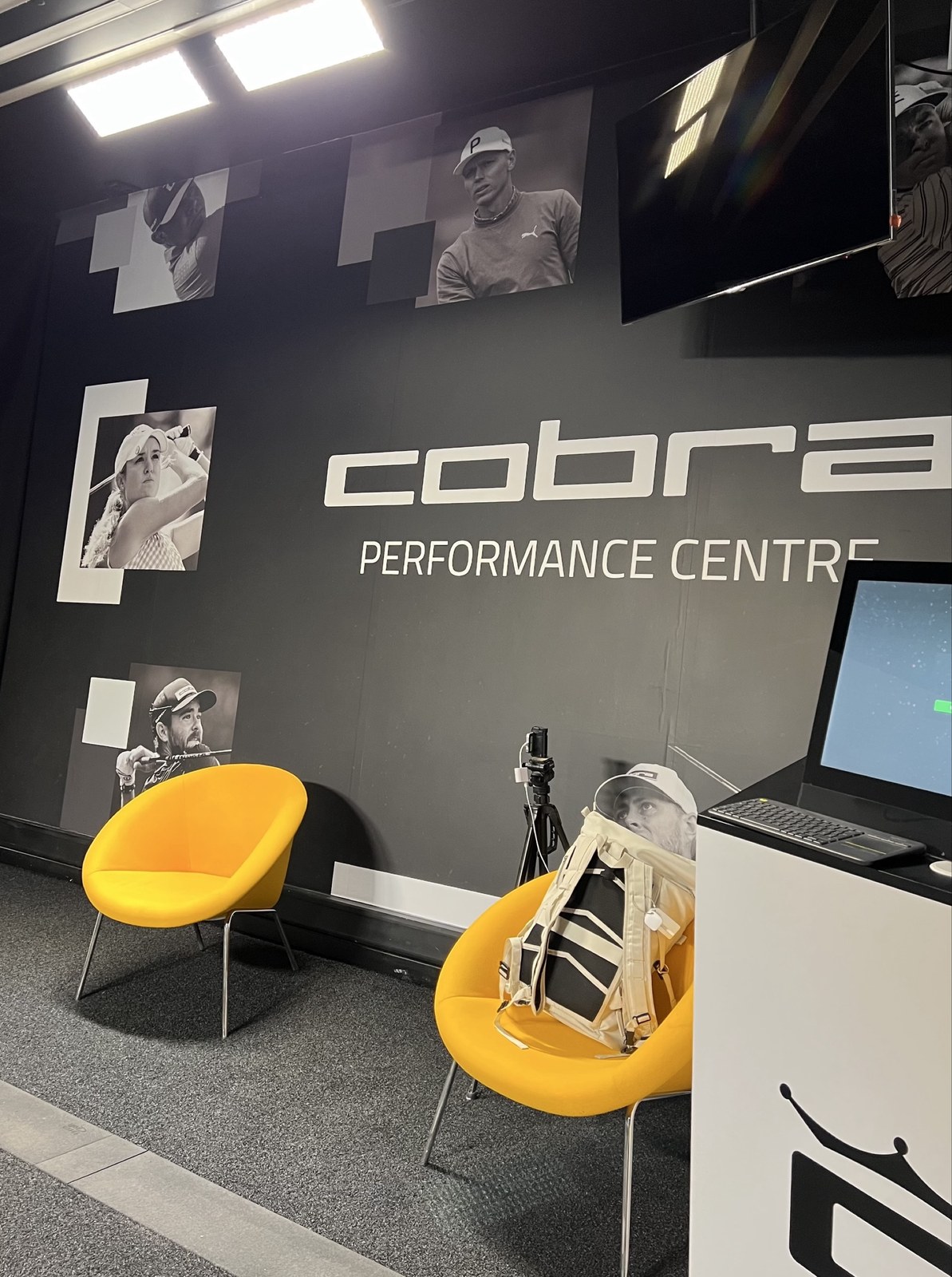 Innenraum des Cobra Performance Center mit gelben Sesseln und Simulator-Bildschirm, an der Wand Fotos von Cobra-Puma-Profis