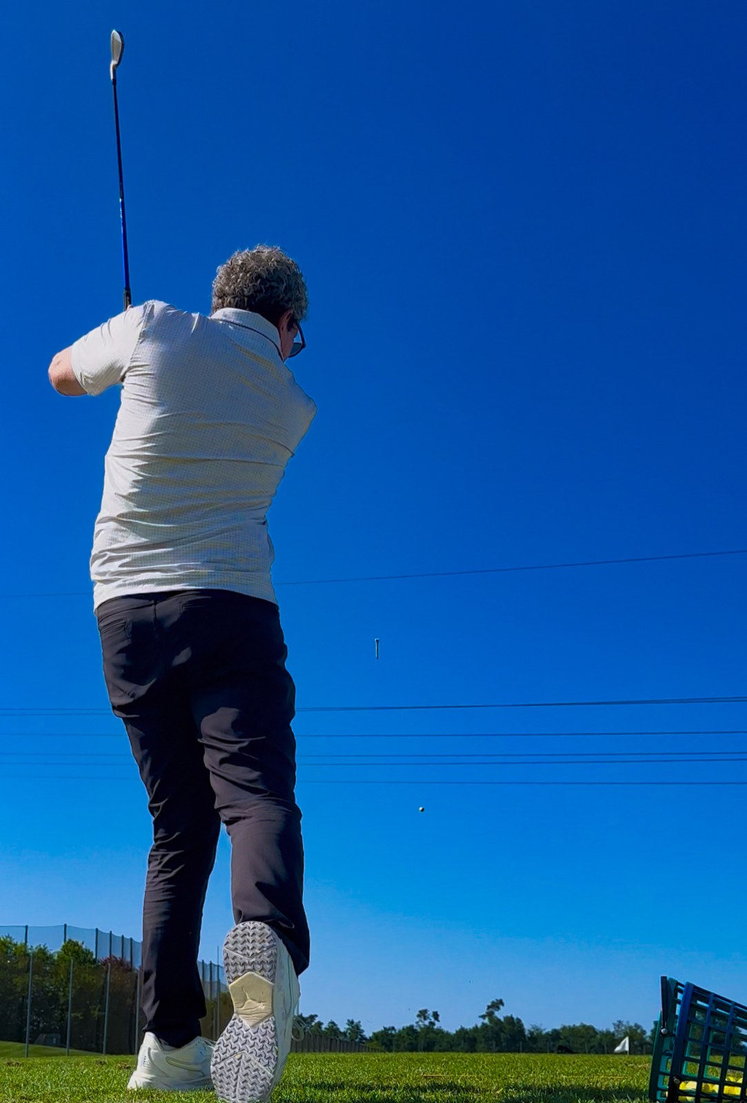 Golfer im Finish des Schwungs auf der Driving Range des Golf-Club Herzogenaurach, der Ball hoch am blauen Himmel