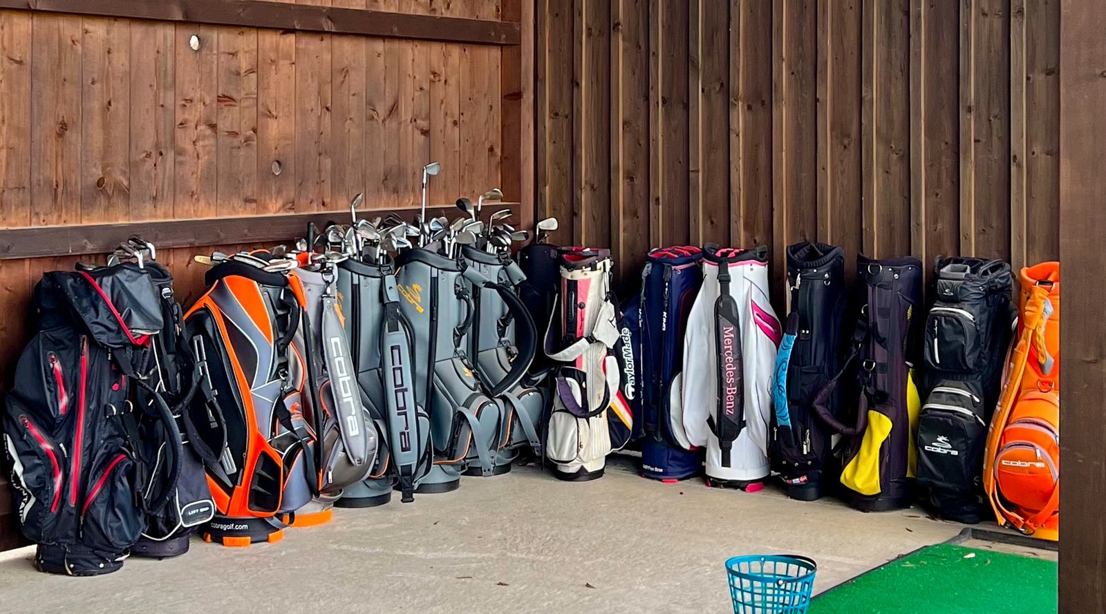 Reihe von Golfbags mit Schlägern an einer Holzwand der Craig Miller Golfschule, davor Trainingsbälle