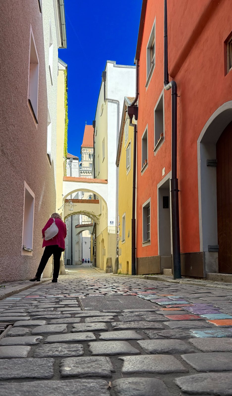 Farbenfrohe Altstadtgasse in Passau mit rosa, gelben und orangen Fassaden und Blick auf den Rathausturm