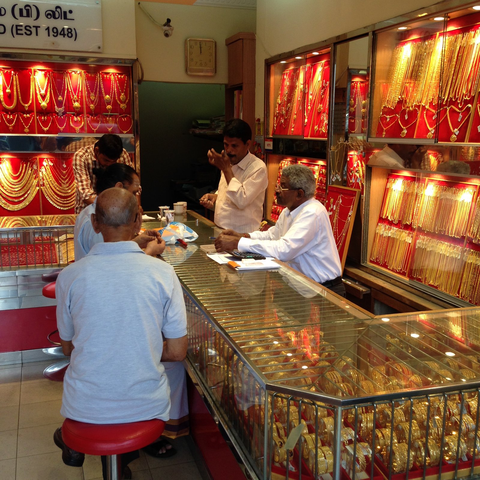Goldschmuckladen in der Kerbau Road in Little India: rot ausgekleidete Vitrinen voller Goldketten und Armreifen, am Glastresen Kunden auf roten Hockern und ein Juwelier mit Taschenrechner