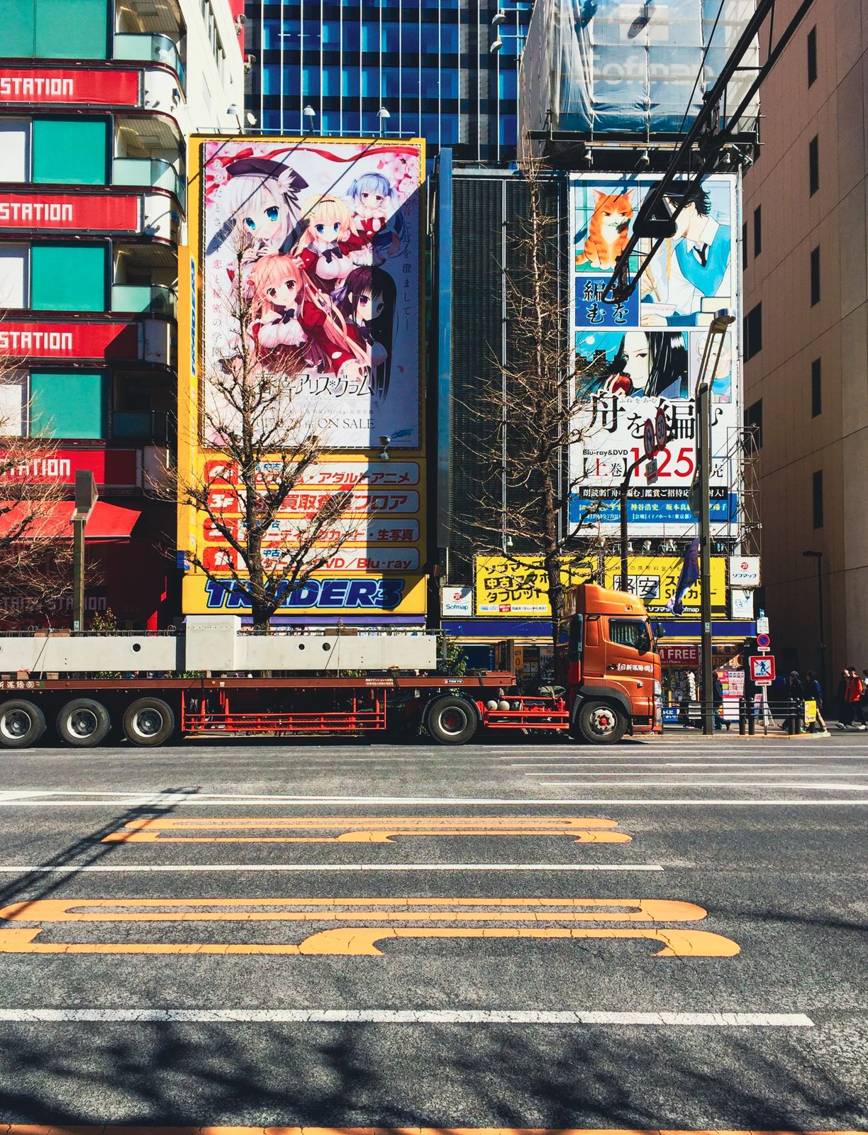 Orangefarbener LKW vor riesigen Anime-Werbetafeln an einer Kreuzung in Akihabara