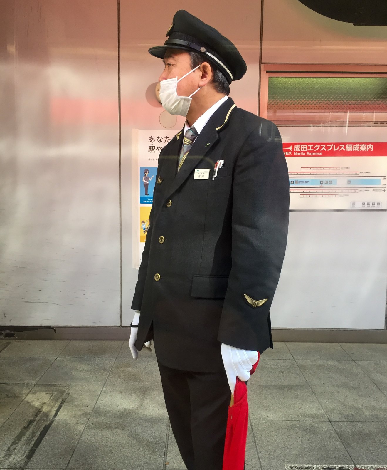 JR-Schaffner in Uniform mit weißen Handschuhen und roter Signalkelle auf einem Tokioter Bahnsteig